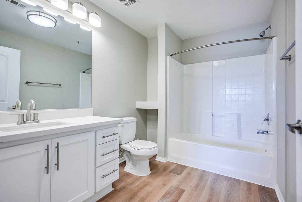 a bathroom with white cabinets and a white toilet next to a white bathtub with a shower