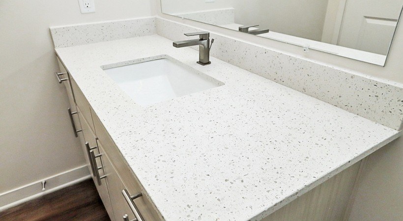 A white speckled countertop with a sink and a mirror above it.