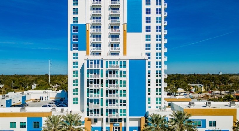 A tall blue and white building stands in front of a row of smaller buildings.