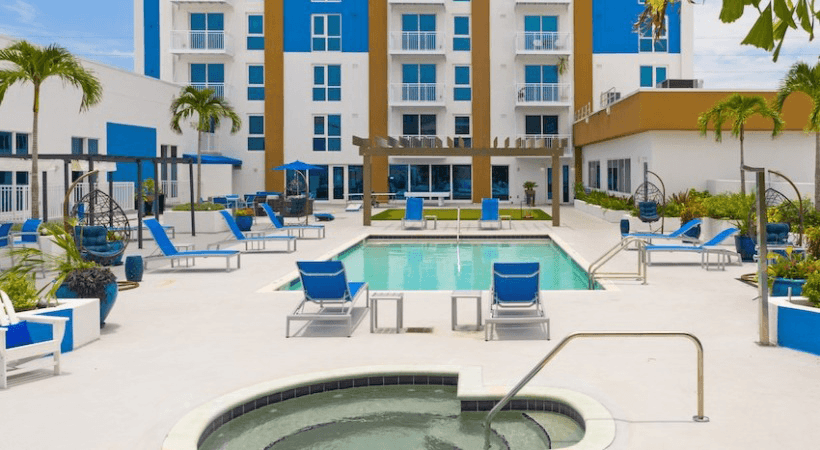 A pool area with a hot tub and lounge chairs in front of a multi-story building.
