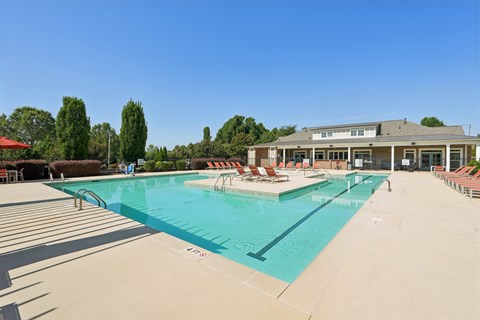 A large swimming pool with lounge chairs and a building in the background.