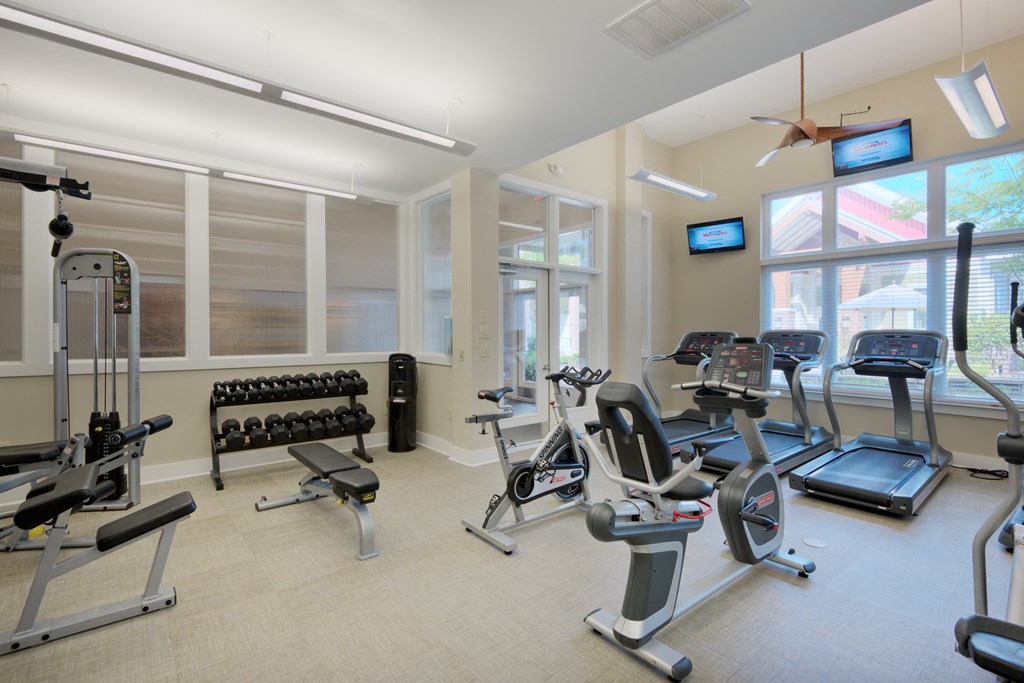 a spacious fitness room with cardio equipment and windows