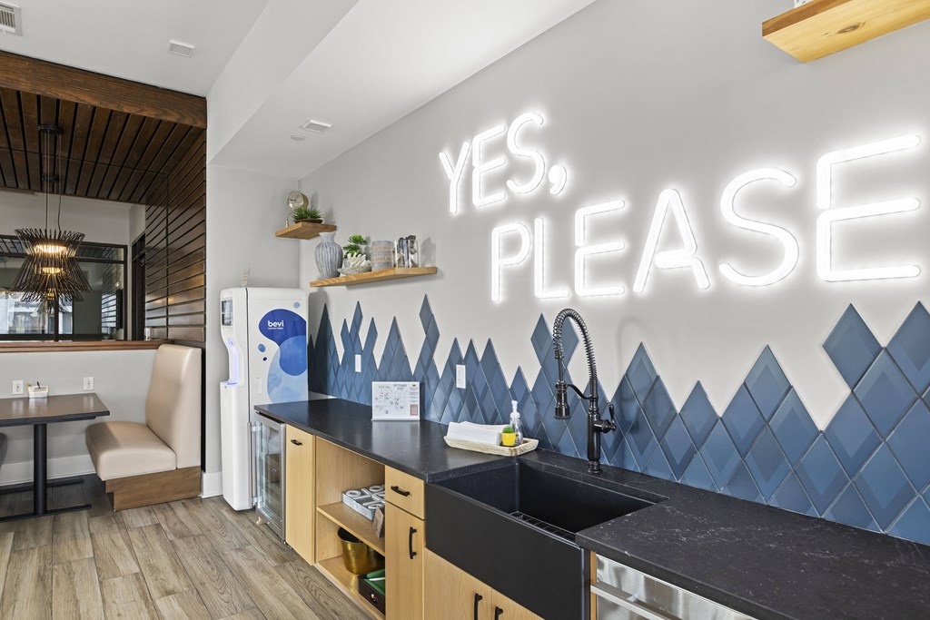 A kitchen with a black counter top and a wall with a neon sign that says "YES. PLEASE.".