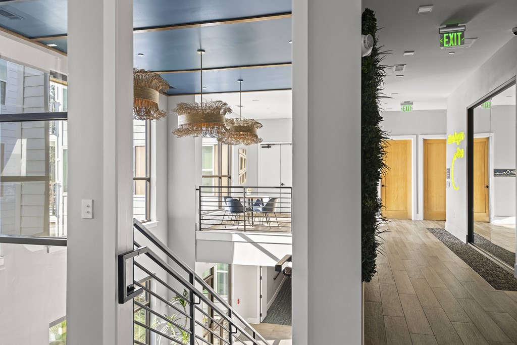A hallway with a staircase and a green exit sign.