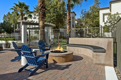 a fire pit with two chairs and a bench in front of a fence
