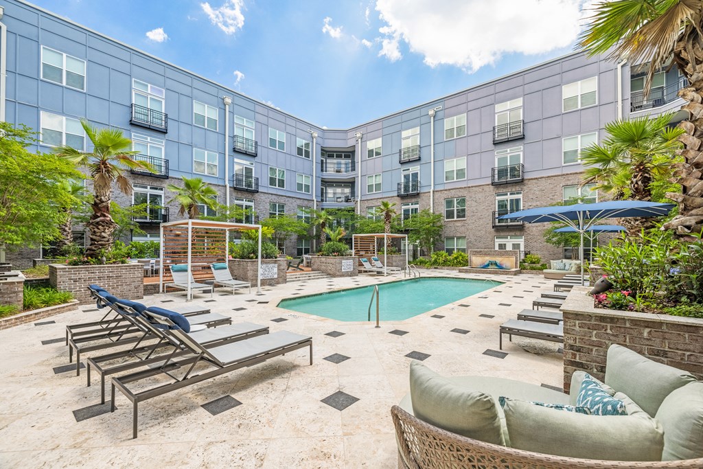a pool with lounge chairs and umbrellas in front of an apartment building