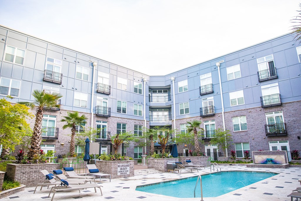 an outdoor swimming pool with chaise lounge chairs and palm trees in front of an apartment building