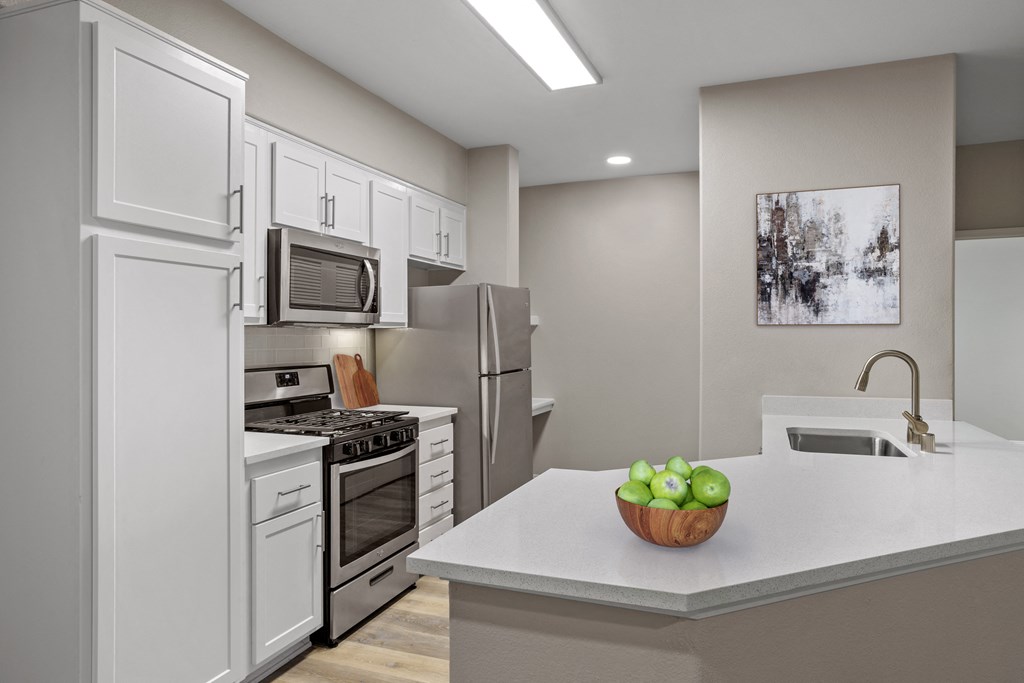 a kitchen with white cabinetry and a white counter top with a bowl of green apples on