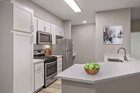 a kitchen with white cabinetry and a white counter top with a bowl of green apples on