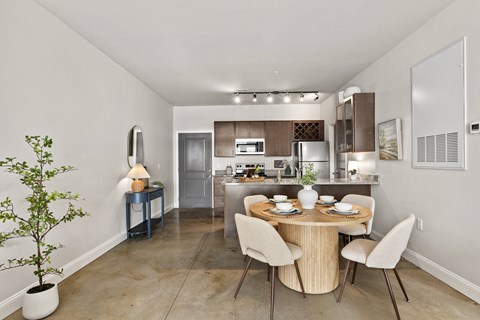 A dining room with a table set for two and a potted plant on the left.