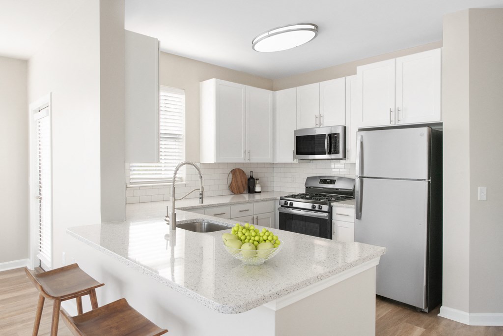 a kitchen with white cabinets and a white island with a bowl of fruit on it