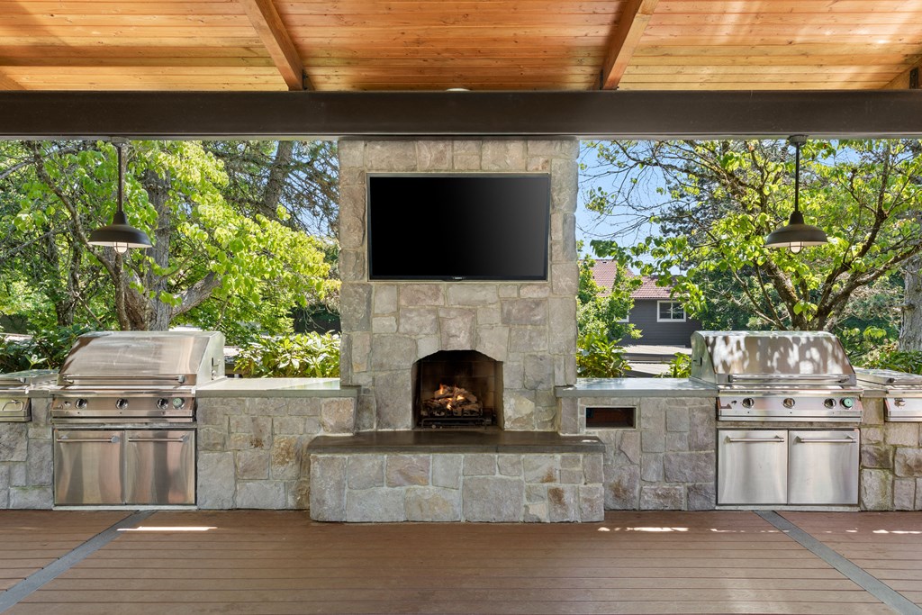 a large outdoor kitchen with a stone fireplace and a tv