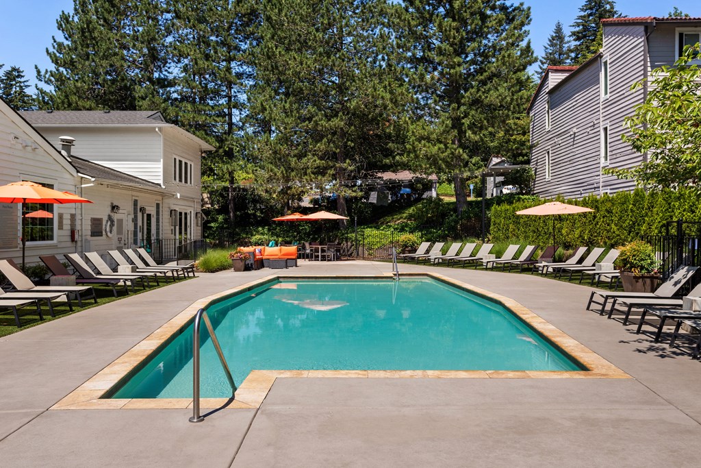 a swimming pool with chairs and umbrellas in front of a house