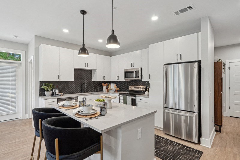 an open kitchen and dining area with a large island and stainless steel refrigerator