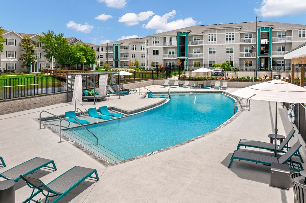 a swimming pool with lounge chairs and umbrellas in front of an apartment building