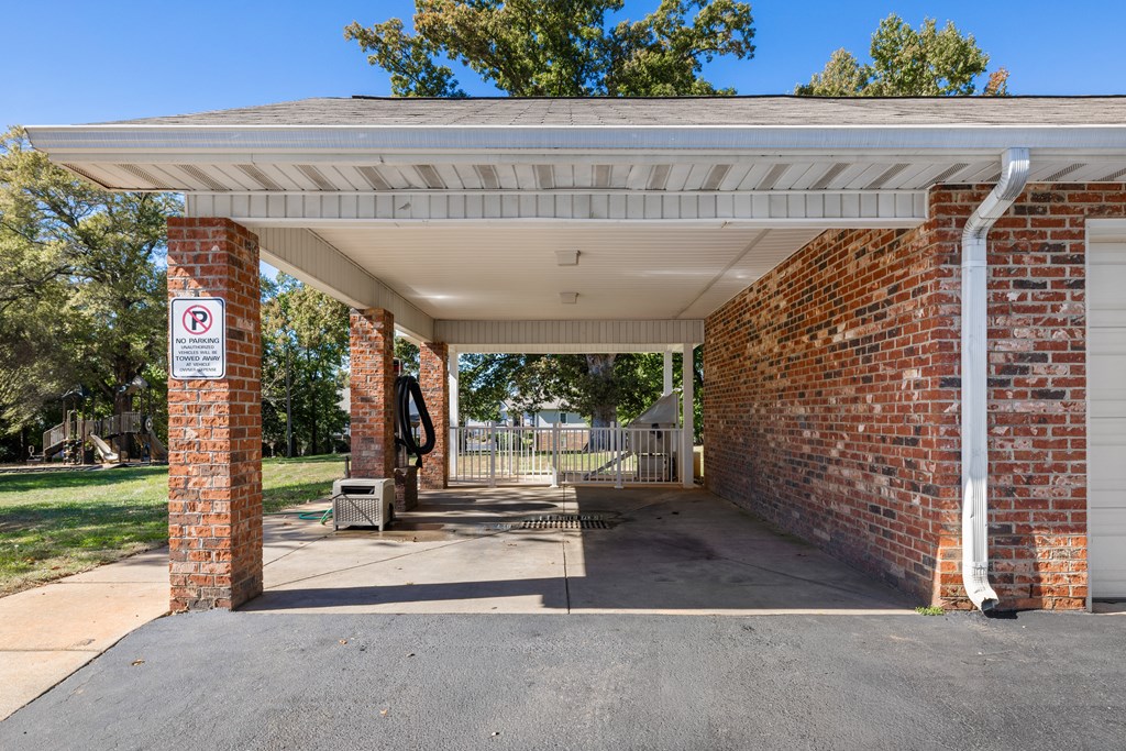 A parking sign is on a brick pillar under a covered parking area.