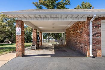 A parking sign is on a brick pillar at the entrance to a covered parking area.
