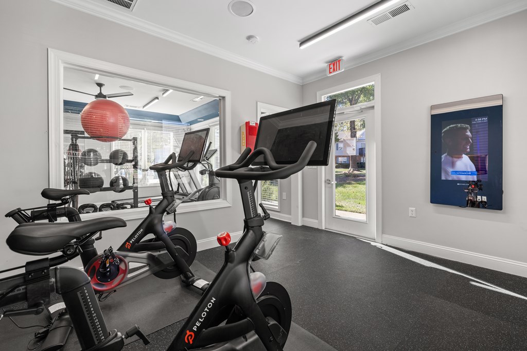 A gym with a row of stationary bikes and a TV screen.