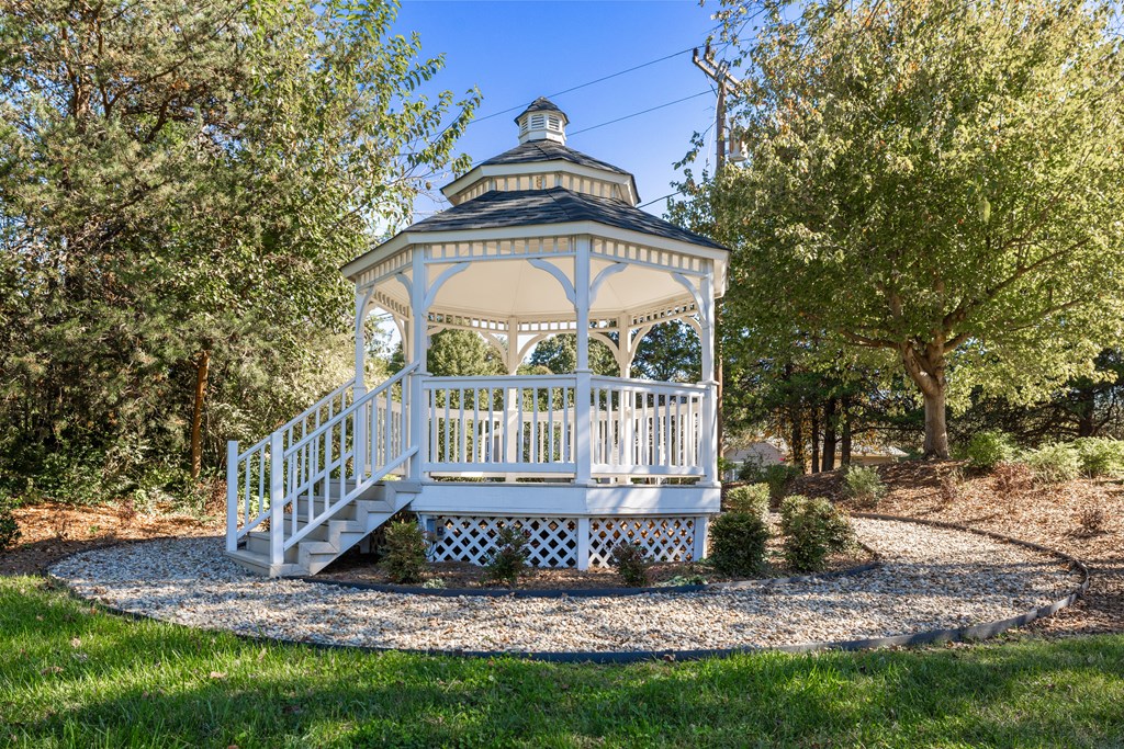 A gazebo with a white railing and steps is surrounded by trees.