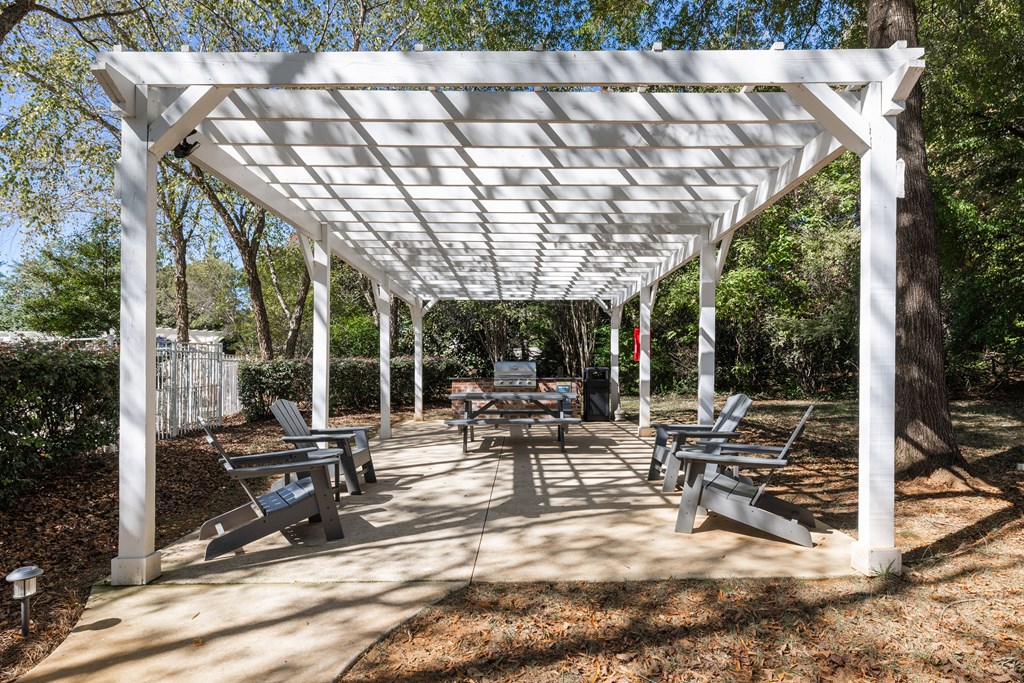 A white pergola with benches is set up in a park.