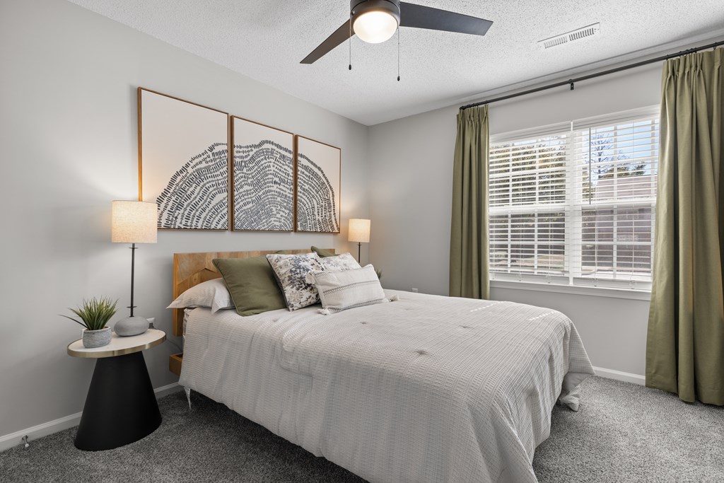A bedroom with a large bed, a ceiling fan, and a wall art piece.