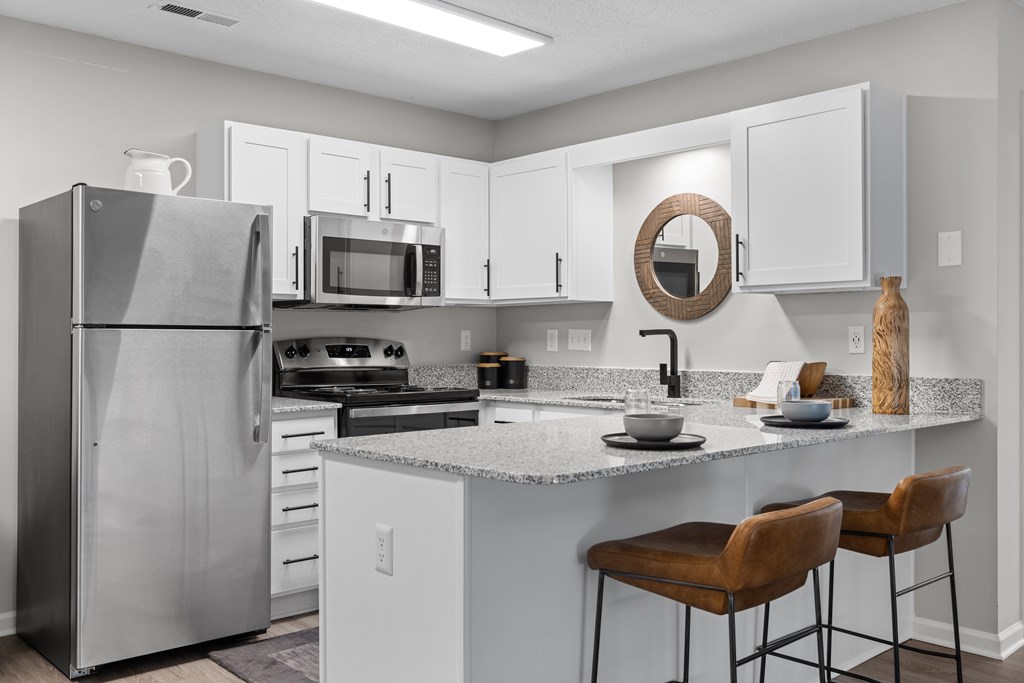 A kitchen with a refrigerator, microwave, oven, and bar stools.