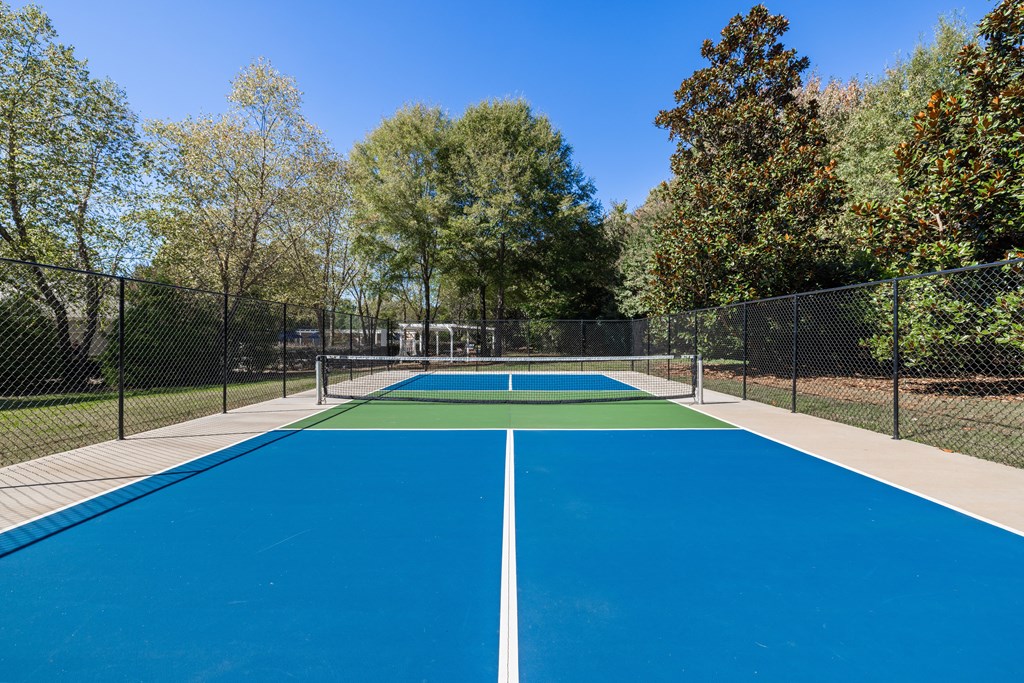 A blue tennis court surrounded by a fence and trees.