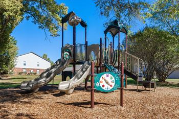 A playground with a slide and a clock on a pole.