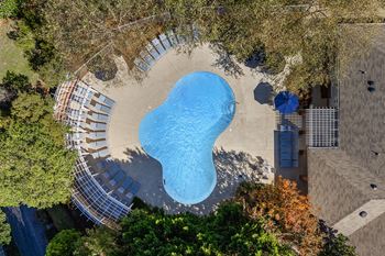 An aerial view of a swimming pool surrounded by trees and a building.
