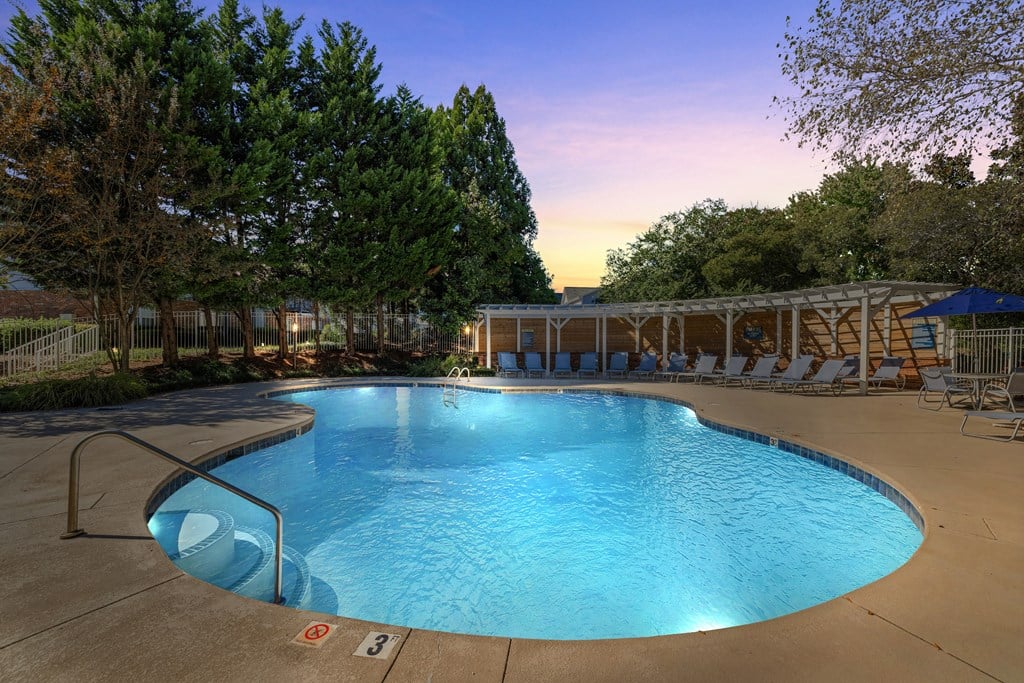 A large outdoor swimming pool surrounded by trees and lounge chairs.