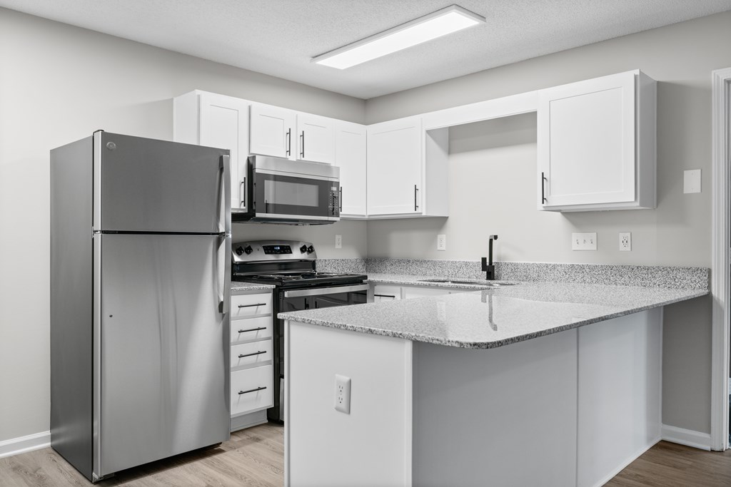 A kitchen with a refrigerator, microwave, oven, and sink.