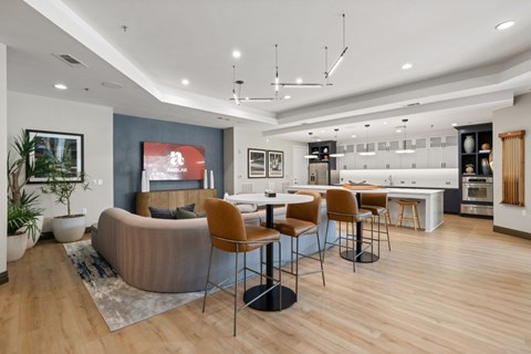 A modern living room with a grey sofa, a wooden dining table and chairs, and a kitchen area in the background.
