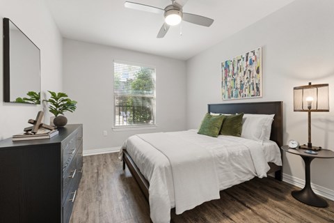 A bedroom with a bed, a dresser, a ceiling fan, and a painting on the wall.