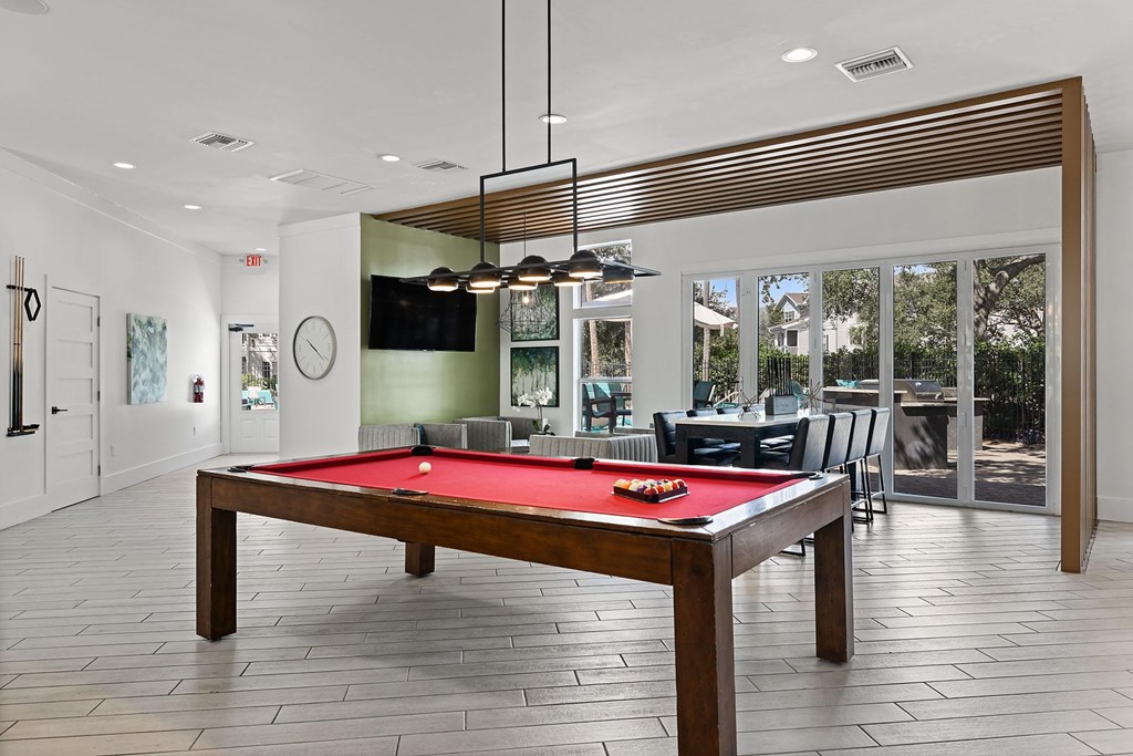 A pool table is in the middle of a room with a television and a clock on the wall.