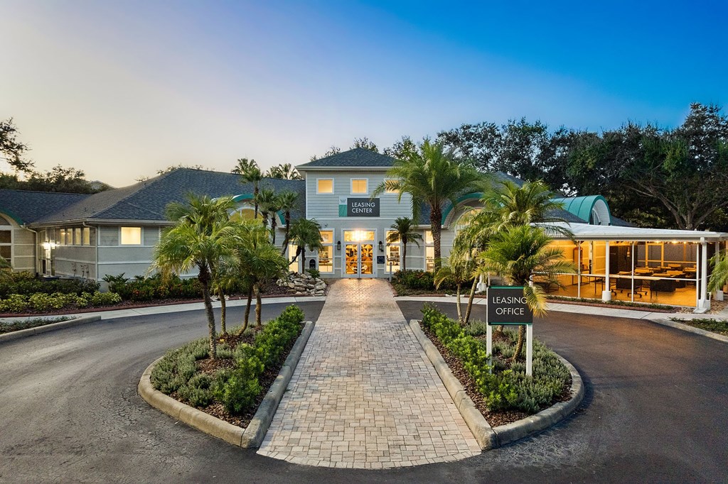 A leasing office is located in a building with a driveway and palm trees.