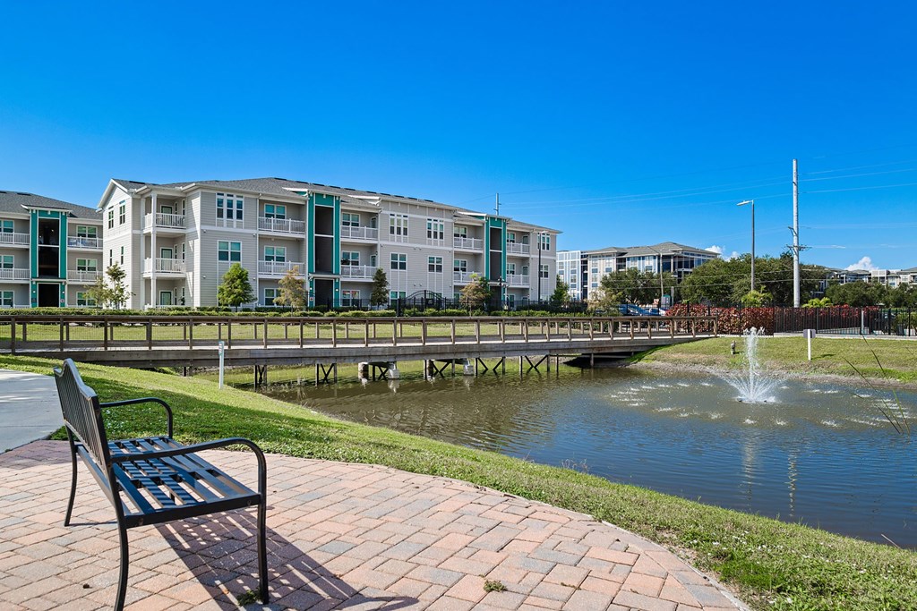 A park with a bench and a fountain in front of apartment buildings.