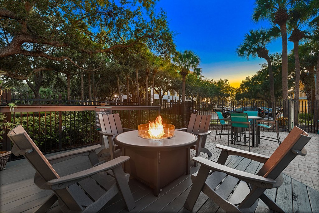 A fire pit sits in the middle of a wooden deck with chairs around it.
