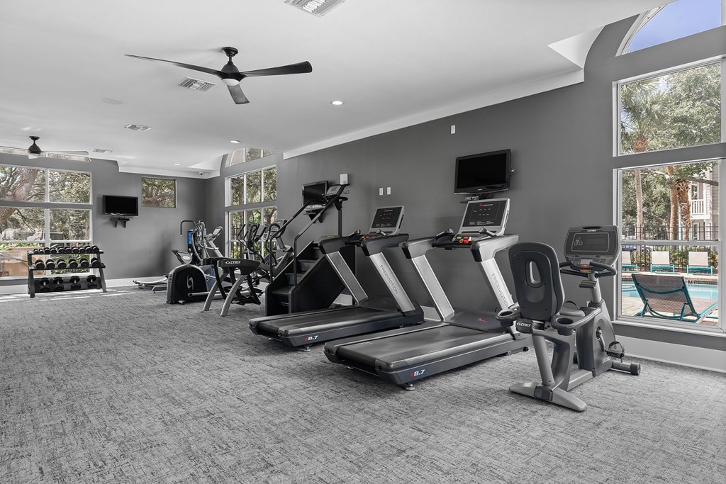 A spacious gym with treadmills, elliptical machines, and a ceiling fan.