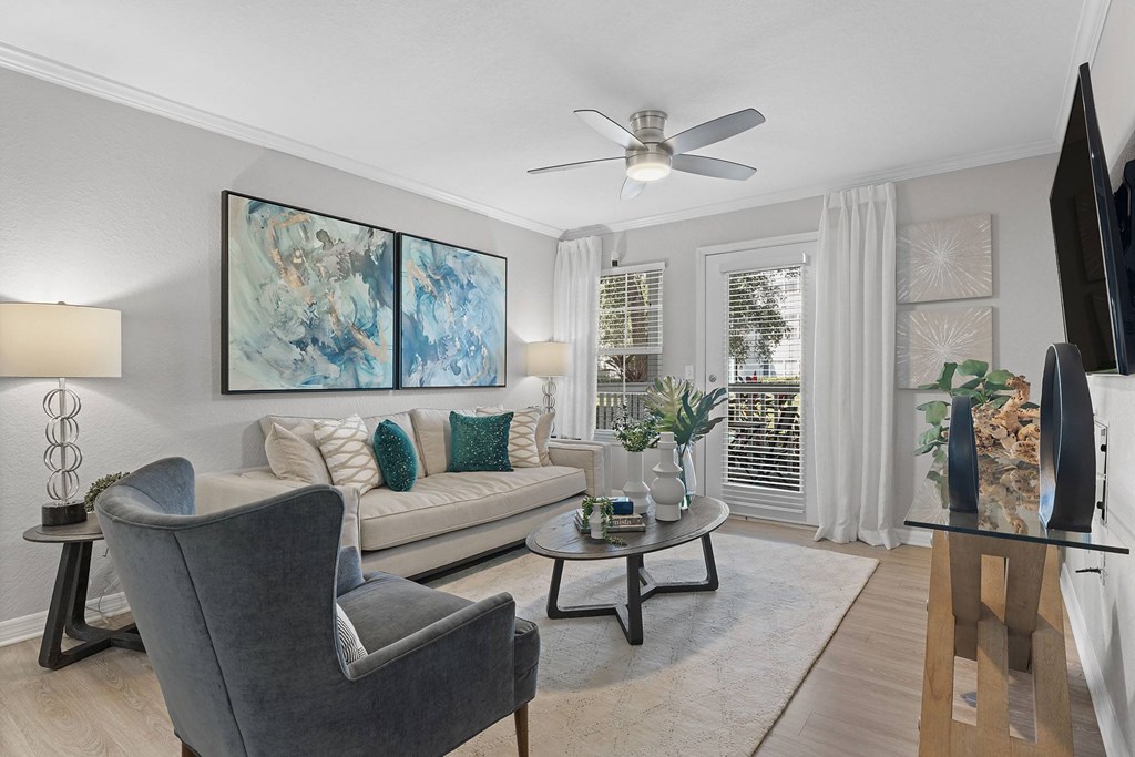 A living room with a grey armchair, a grey sofa, a glass coffee table, a television, and a painting on the wall.