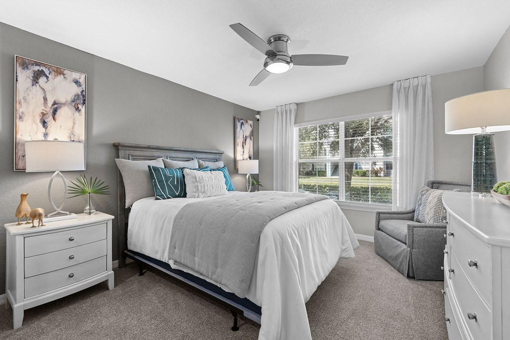 A bedroom with a large bed, a ceiling fan, and a window with white curtains.