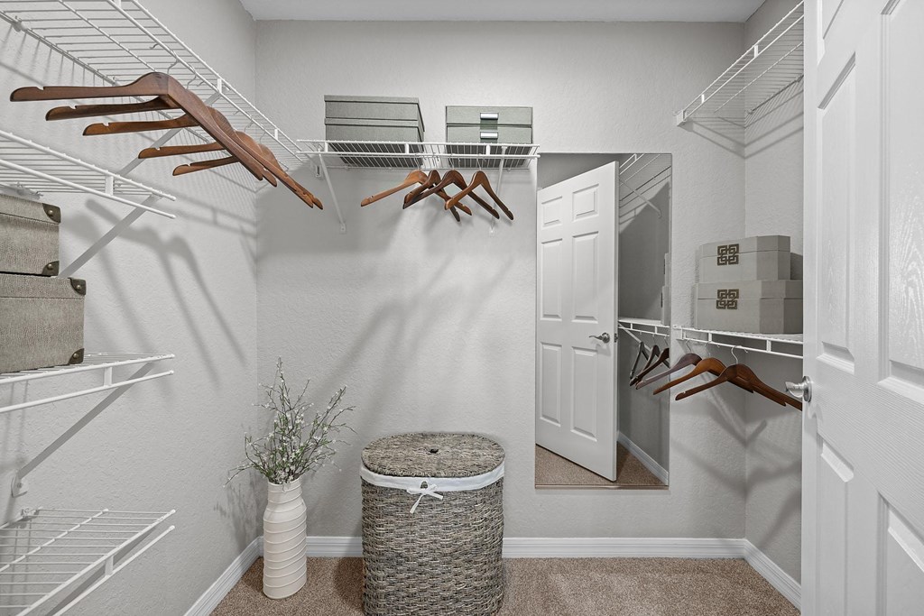 A white closet with clothes hanging on shelves and a basket on the floor.