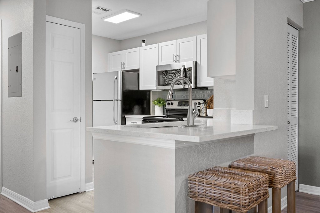 A kitchen with white cabinets and a white island with two stools.