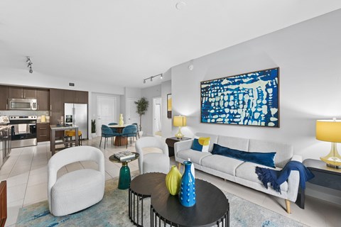 A modern living room with a white sofa, a blue and white abstract painting on the wall, and a black coffee table with yellow vases.