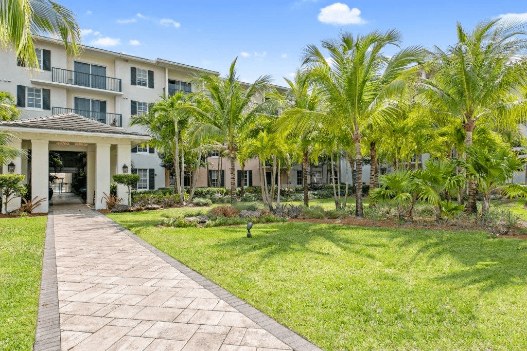 A walkway leads to a building with a balcony and palm trees in the foreground.