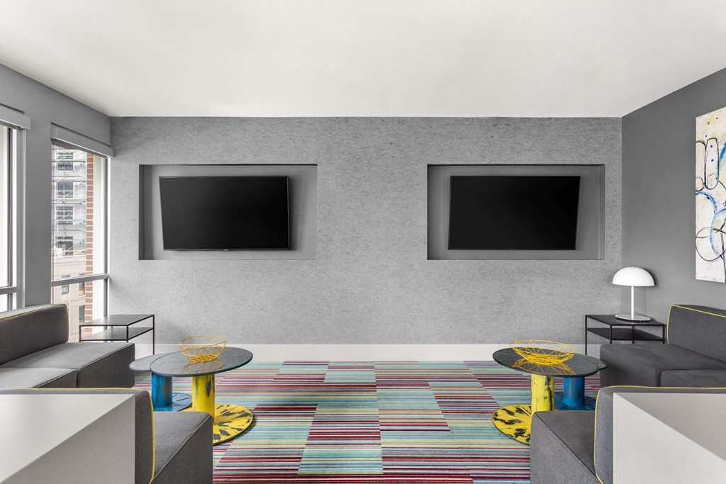 a living room with couches and tables and two televisions on the wall