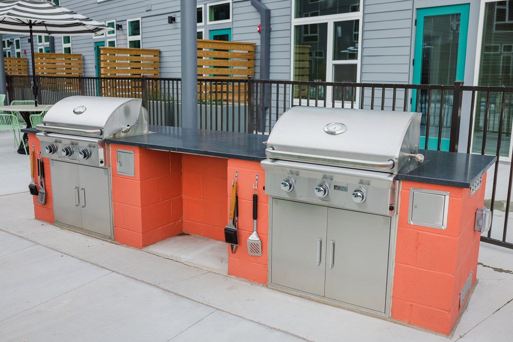 three stainless steel stoves and two orange and gray barbecue grills on a sidewalk