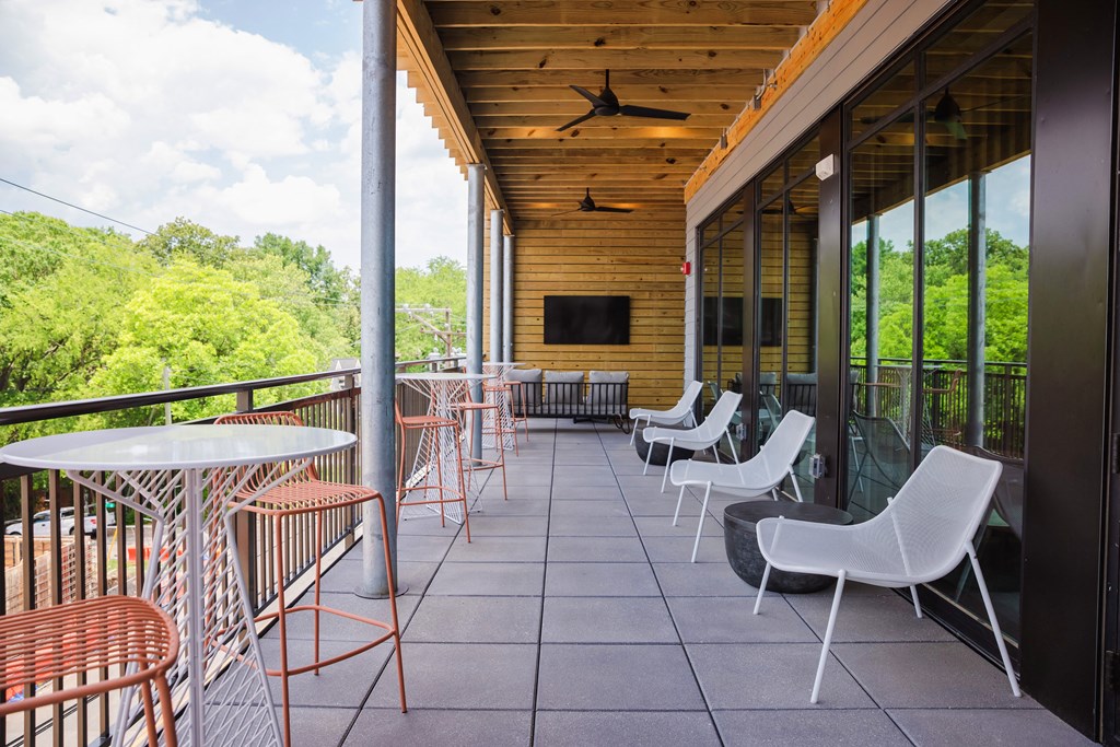 a balcony with chairs and tables and a wooden building with trees