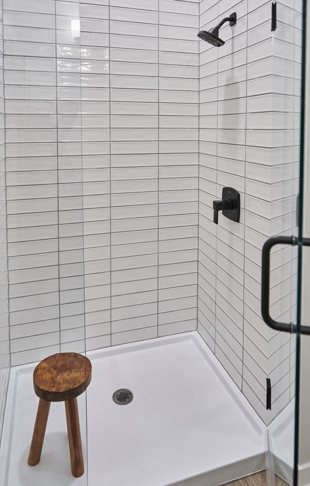 a white tiled shower with a wooden stool in a bathroom