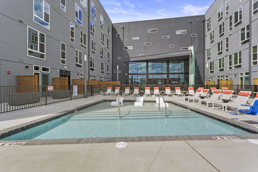 an apartment pool with chairs and a building in the background