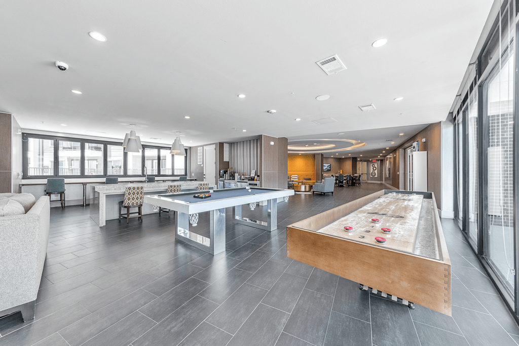 A shiny billiard table with red balls is in the middle of a room with a grey floor and a white sofa.